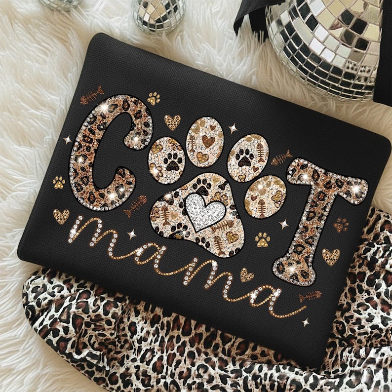 May include: Black tote bag with the words "Cool Mama" in a leopard print design, with paw prints and hearts. The bag is decorated with glitter and small fish bone and paw print accents.