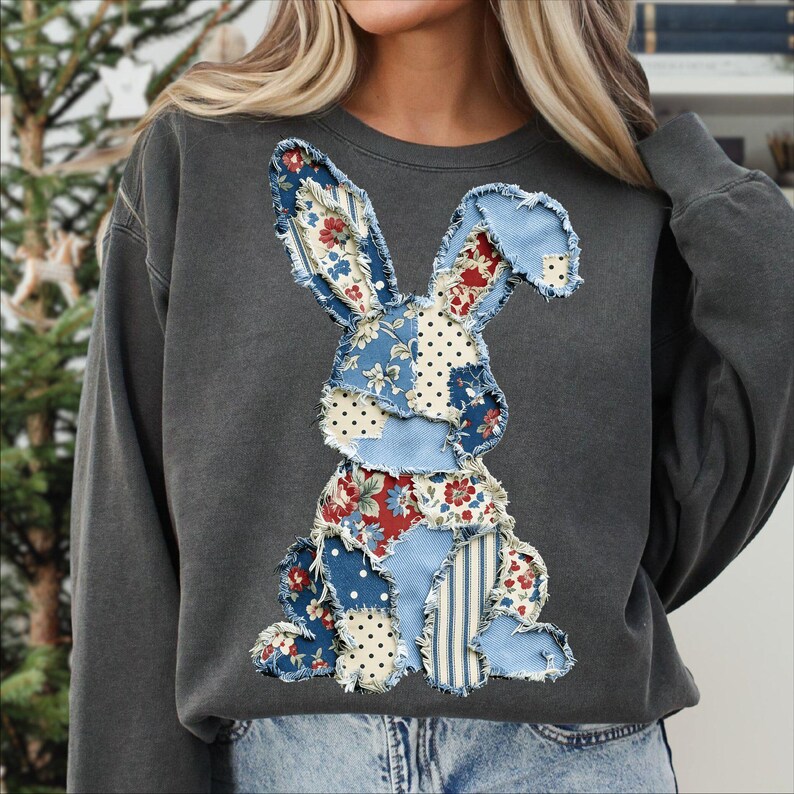 May include: Dark gray sweatshirt featuring a patchwork bunny design. The bunny is made of various fabrics with floral, polka dot, and striped patterns in blue, red, and white. The sweatshirt has a crew neck and long sleeves.