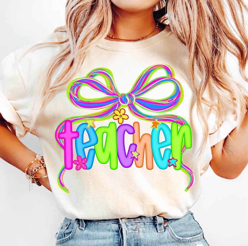 May include: Cream-colored t-shirt with a colorful bow and the word "teacher" in vibrant letters. The design includes flowers and stars, creating a cheerful and playful aesthetic. A perfect gift for educators.