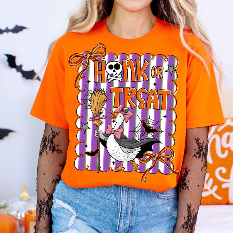 May include: Orange t-shirt with a Halloween-themed graphic. The design features the text "Honk or Treat" with a skull and crossbones, a cartoon goose in a witch costume, bats, and a broom. The graphic is set against a purple and white striped background.