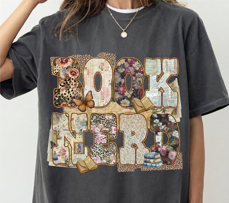 May include: Dark gray t-shirt with the words "BOOK NERD" in a collage of floral patterns, leopard print, and vintage paper. A butterfly and small books are also featured in the design.
