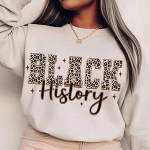 May include: Cream-colored sweatshirt with the words "BLACK HISTORY" in a bold, leopard print font. The word "History" is written in a cursive font below the main text, with star accents.