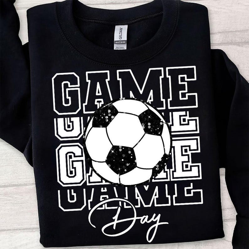 Może przedstawiać: Czarna bluza z napisem "GAME DAY" w białych literach i grafiką piłki nożnej. Piłka nożna jest czarno-biała z brokatowymi akcentami. Bluza marki Gildan.