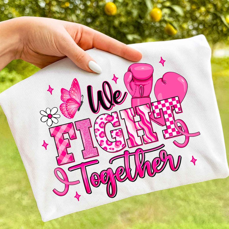 May include: White t-shirt with a pink design featuring a butterfly, boxing gloves, and the words "We Fight Together." The text is in various pink fonts and patterns, including a checkered design. Pink stars and a daisy complete the design.