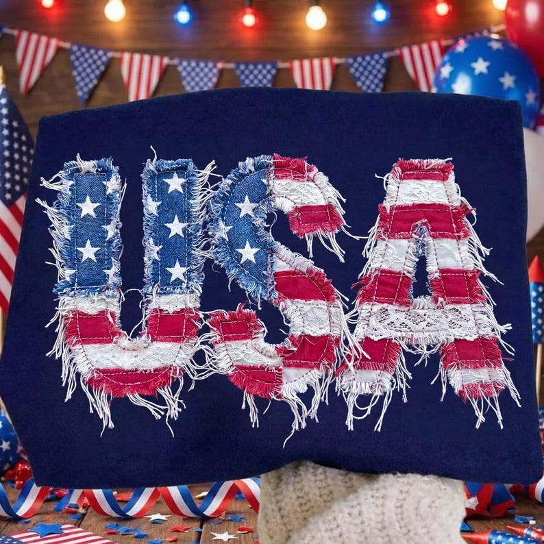 Op de afbeelding: Marineblauw shirt met het woord "USA" op de voorkant. De letters zijn gemaakt van denim en rood-wit gestreepte stof, met witte kanten accenten. De letters hebben een gerafelde rand.