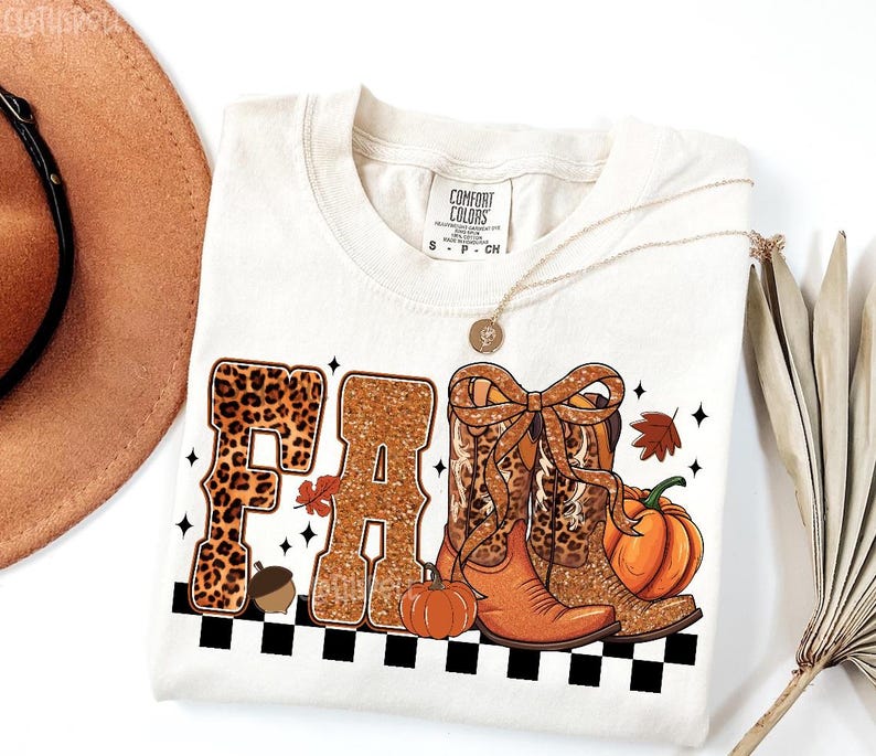 Peut inclure: T-shirt cr&egrave;me avec un motif "FALL". Les lettres sont d&eacute;cor&eacute;es d'imprim&eacute; l&eacute;opard et de paillettes. Le motif comprend des bottes de cowboy, des citrouilles et un gland. Un collier dor&eacute; et un chapeau marron sont &eacute;galement visibles.
