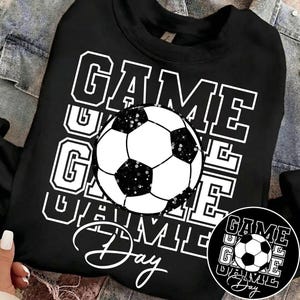 Może przedstawiać: Czarna bluza z białym nadrukiem piłki nożnej i napisem "GAME DAY" w ułożonym wzorze. Piłka nożna ma czarno-białe panele z brokatowymi akcentami. Mniejsza wersja projektu znajduje się po prawej stronie u dołu.