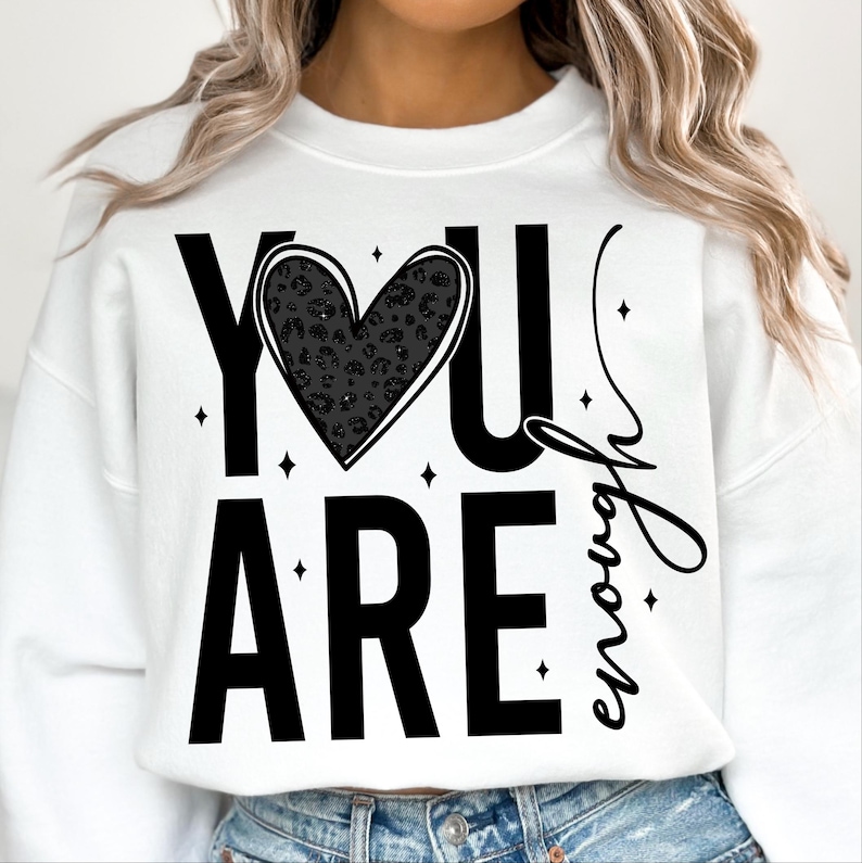 Peut inclure: Sweat-shirt blanc avec un texte noir qui dit "YOU ARE enough" avec un c&oelig;ur noir imprim&eacute; l&eacute;opard au milieu.