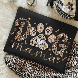 May include: Black laptop sleeve with the words "Dog mama" in a sparkly gold font. The word "Dog" is designed with leopard print and paw prints. The paw print design includes a heart.