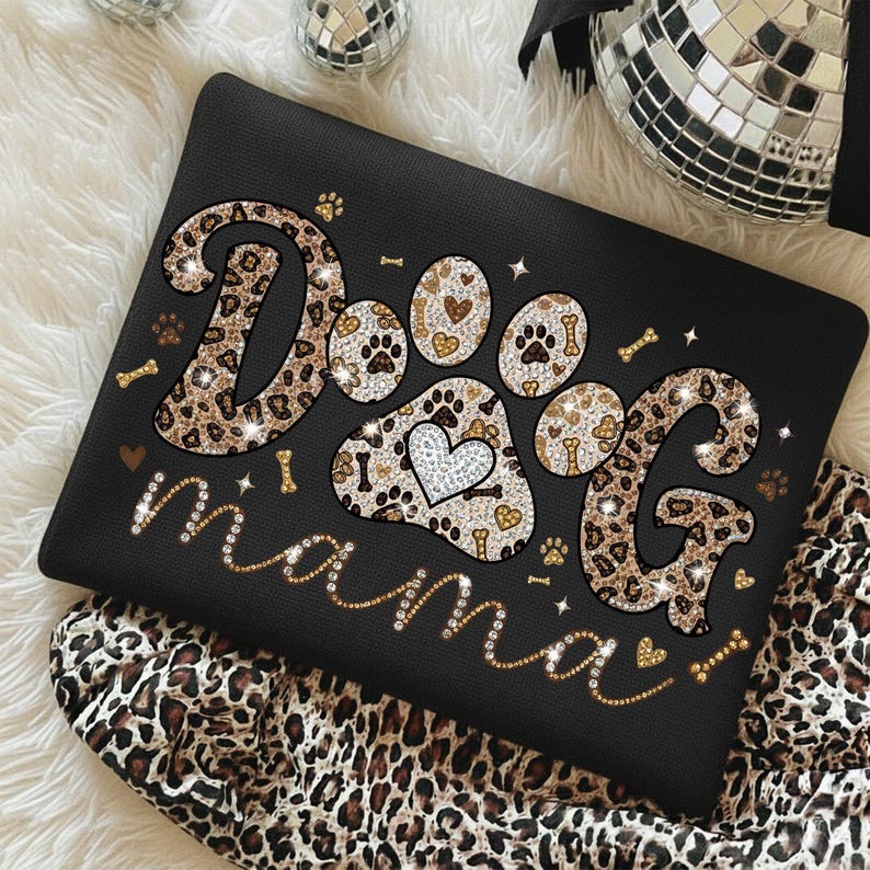 May include: Black laptop sleeve with the words "Dog mama" in a sparkly gold font. The word "Dog" is designed with leopard print and paw prints. The paw print design includes a heart.