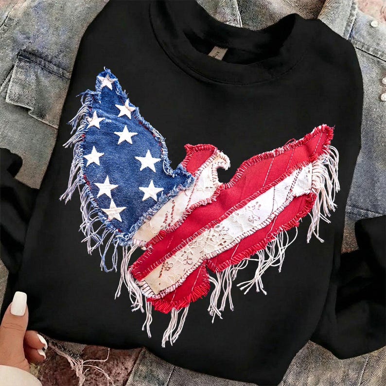 May include: Black sweatshirt featuring a patriotic design. The design incorporates elements of the American flag, with a blue denim patch displaying white stars and red and white striped sections with lace detailing. The edges have a frayed, distressed look.