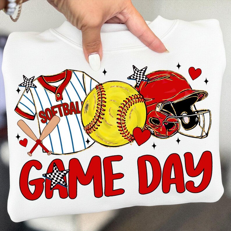 May include: White sweatshirt with a softball design. It features a yellow softball, red helmet, baseball bat, and a jersey with the word "SOFTBALL". The phrase "GAME DAY" is written in red. Decorated with hearts and stars.