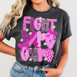 May include: Dark gray t-shirt with the words "FIGHT HOPE CURE" in pink, white, and black patterns. The design includes a pink ribbon, bows, and daisy accents, promoting breast cancer awareness.