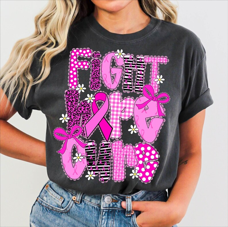 May include: Dark gray t-shirt with the words "FIGHT HOPE CURE" in pink, white, and black patterns. The design includes a pink ribbon, bows, and daisy accents, promoting breast cancer awareness.
