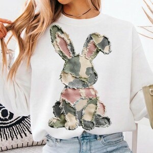 May include: White sweatshirt featuring a patchwork bunny design in shades of green, pink, and beige. The bunny is centered on the front of the long-sleeved top. The sweatshirt is made of a soft material.