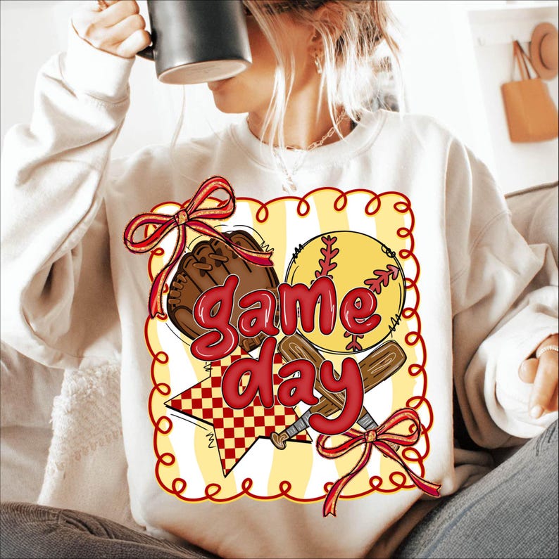 Puede incluir: Sudadera crema con un dise&ntilde;o de b&eacute;isbol. El gr&aacute;fico incluye una pelota de b&eacute;isbol, un guante y bates cruzados, con las palabras "Game Day" en rojo. El dise&ntilde;o est&aacute; enmarcado por un borde amarillo con detalles rojos.