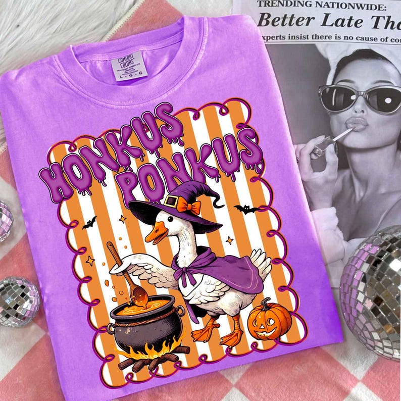 May include: A purple Comfort Colors t-shirt featuring a Halloween-themed graphic. The design includes the words "HONKUS PONKUS" in purple, a goose wearing a witch hat and cape, a cauldron, and a pumpkin. The shirt is a comfortable, casual wear.