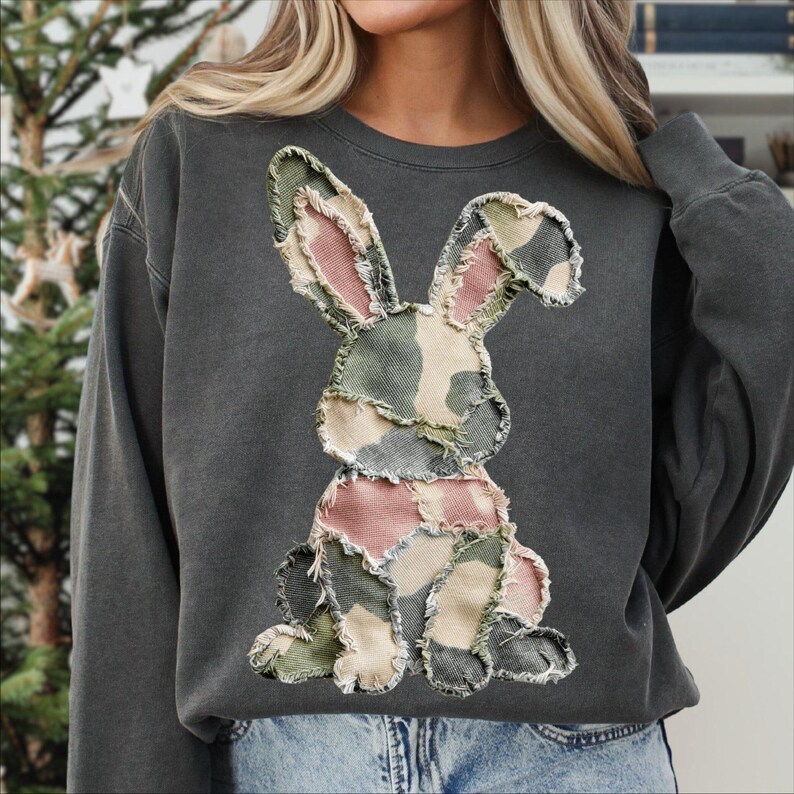 May include: Dark gray sweatshirt featuring a patchwork bunny design. The bunny is made of fabric in shades of pink, green, and beige, with a distressed, frayed edge. The sweatshirt has a crew neck and long sleeves, suitable for casual wear.