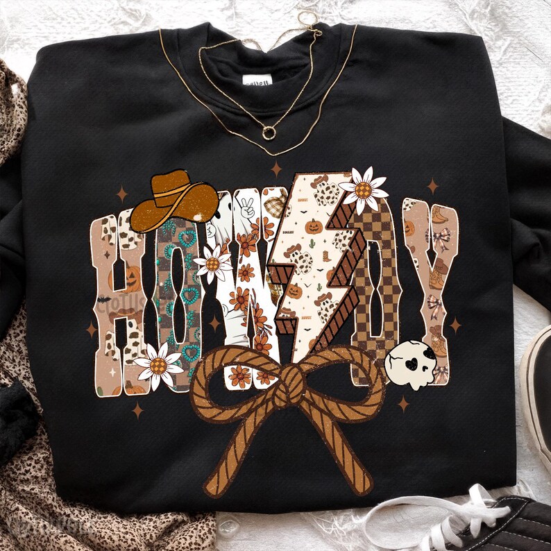 May include: Black sweatshirt featuring the text "HONKY TONK" in a western design. The design incorporates a cowboy hat, lightning bolt, flowers, and a rope bow. The sweatshirt has a casual, country aesthetic.