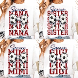 May include: White sweatshirt featuring a soccer ball bow design. The word "Soccer" is written in blue script above the bow. Below the bow, the word "NANA" is repeated in a red, block font.