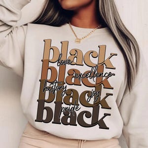 May include: Cream-colored sweatshirt with the words "black love, black excellence, black history, black joy, black pride" in brown and black lettering. The sweatshirt is a casual style.