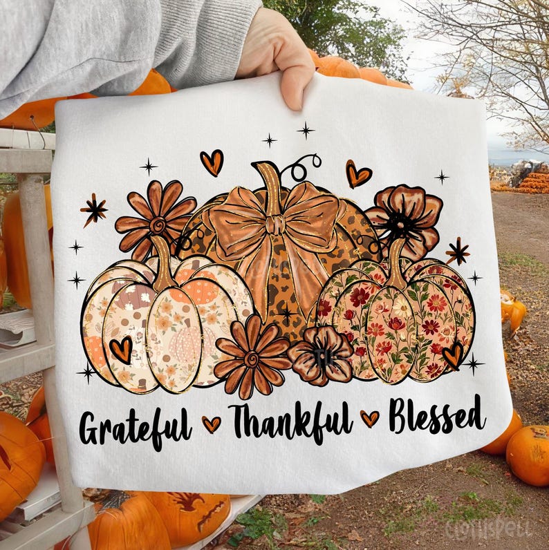 May include: White sweatshirt featuring a fall-themed design with pumpkins, flowers, and hearts. The pumpkins have floral and leopard print patterns. The text "Grateful Thankful Blessed" is printed at the bottom.
