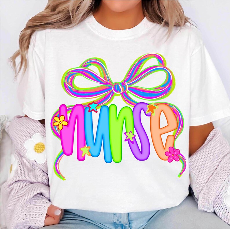 May include: White t-shirt with the word "NURSE" in bright, bubble letters, decorated with a rainbow bow and star and flower details. The design is colourful and appealing, suitable for healthcare workers.