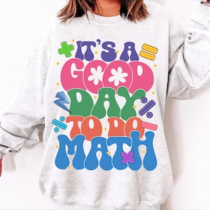 May include: A white sweatshirt with the text "It's a good day to do math" in colorful, retro-style lettering. The letters are decorated with various mathematical symbols.