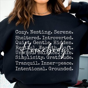 Peut inclure: Sweat-shirt noir avec du texte blanc qui dit "Cozy. Nesting. Serene. Sheltered. Introverted. Quiet. Gentle. Hidden. Restful. Warmth. Soft. Unwind. Balance. Safe. Simplicity. Gratitude. Tranquil. Inner-peace. Intentional. Grounded."