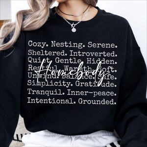 Peut inclure: Sweat-shirt noir avec du texte blanc qui dit "Cozy. Nesting. Serene. Sheltered. Introverted. Quiet. Gentle. Hidden. Restful. Warmth. Soft. Homebody. Unwind. Balance. Safe. Simplicity. Gratitude. Tranquil. Inner-peace. Intentional. Grounded."