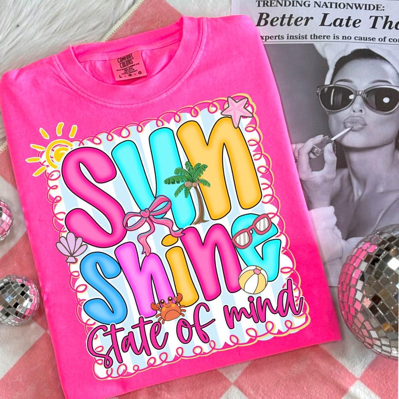 K&ouml;nnte beinhalten: Ein leuchtend pinkfarbenes T-Shirt mit dem Schriftzug "Sunshine State of Mind" in einem bunten, blasenartigen Design. Die Grafik enth&auml;lt eine Sonne, eine Palme, eine Sonnenbrille und andere Sommerelemente.