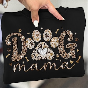 May include: Black sweatshirt with the words "DOG mama" in a sparkly, decorative font. The word "DOG" is designed with a leopard print pattern and paw prints. A paw print design with a heart is in the center.