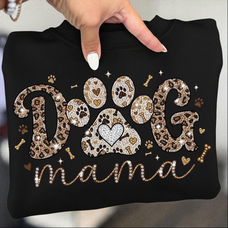 May include: Black sweatshirt with the words "DOG mama" in a sparkly, decorative font. The word "DOG" is designed with a leopard print pattern and paw prints. A paw print design with a heart is in the center.
