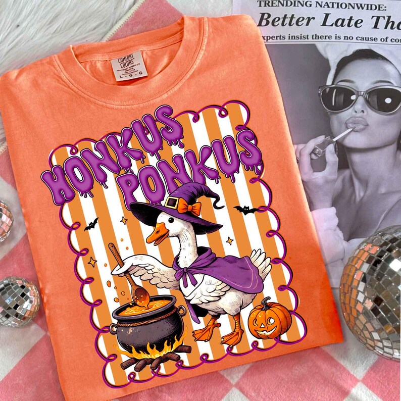 May include: Orange Comfort Colors sweatshirt with a Halloween-themed graphic. The design features a goose wearing a witch hat and cape, stirring a cauldron. The text "HONKUS PONKUS" is displayed above the goose.