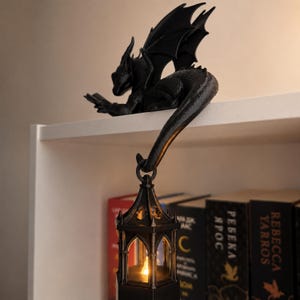 Black 3D printed reading dragon displayed beside books with a glowing hanging lantern for fantasy shelf decor.