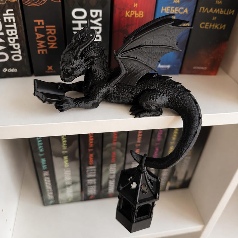 Fantasy bookshelf decor featuring a black reading dragon with wings and a lit lantern hanging from its tail.