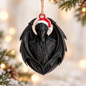 Peut inclure: Une décoration suspendue noire représentant le buste sculpté d'une silhouette dotée de grandes ailes, portant un bonnet de Père Noël rouge et blanc. La figurine présente des traits détaillés et un vêtement texturé, avec une boucle en ficelle.