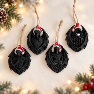 May include: Four black, winged, humanoid ornaments, each wearing a small red and white Santa hat. The figures are sculpted in relief with intricate details and hang from thin, light brown twine loops, arranged in a group against a light background.