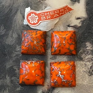 May include: Four square buttons with a glossy orange and dark grey marbled pattern. Above the buttons is a torn white paper label with an orange graphic and the text CHERRY BRAND in white capital letters, featuring a small flower icon.