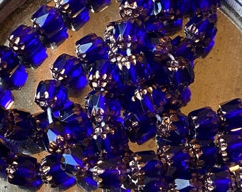 May include: Close-up of strands of faceted, deep blue beads with gold-colored metal accents. The beads are clustered together, reflecting light and creating a sparkling effect. The beads are likely for jewelry making.