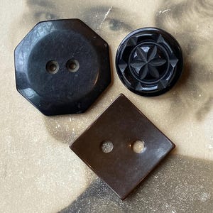 May include: Three vintage buttons in shades of brown and black. The buttons include an octagonal button with two holes, a round button with a starburst design, and a square button with two holes.