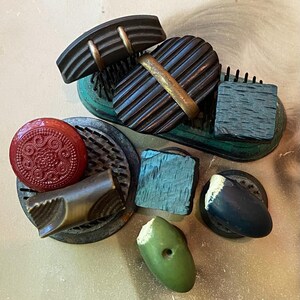 May include: A collection of vintage buttons in various shapes, sizes, and colors. The buttons include a red floral design, a dark blue ridged button, and a green oval button. Some buttons have metal accents.
