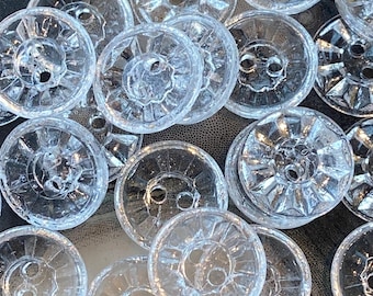 May include: A collection of clear glass buttons with a raised, textured design. The buttons have two holes and are arranged in a random pattern.