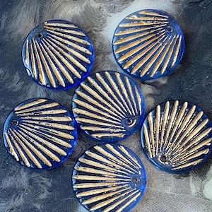 May include: Six round, blue glass beads with a fan-like design in gold. Each bead has a small hole for stringing. The beads are arranged on a patterned surface, showcasing their intricate details and color contrast.