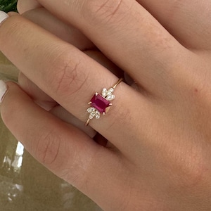 May include: A gold ring with a red gemstone and small white gemstones. The ring is on a person's finger.