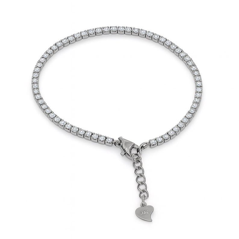 Puede incluir: Una pulsera de tenis plateada con una fila de piedras preciosas redondas y transparentes. La pulsera tiene un cierre seguro y una cadena ajustable. Las piedras preciosas est&aacute;n espaciadas uniformemente y reflejan la luz. Se muestra sobre fondo blanco.