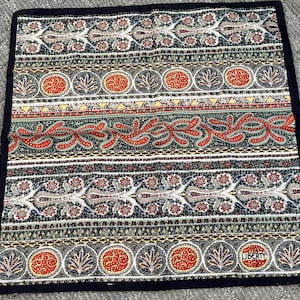 May include: A square fabric handkerchief featuring a multi-colored horizontal striped pattern with floral, paisley, and geometric motifs in shades of red, blue, green, and yellow, finished with a solid black border and the word LIBERTY printed.