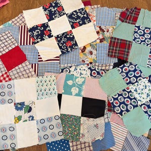 May include: A collection of square fabric quilt blocks featuring a variety of patterns including red and white gingham, blue and white floral prints, plaid, polka dots, and solid white squares arranged in a grid pattern across the surface.