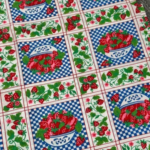 May include: A fabric featuring a repeating grid pattern of white and blue checkered squares containing illustrations of white bowls filled with red strawberries, alternating with vertical panels of green strawberry vines and pink flowers.