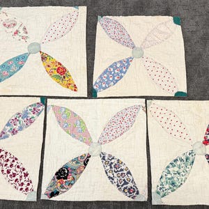 May include: Five vintage quilt blocks with a pinwheel design. Each block features four petal-shaped sections in various floral and patterned fabrics, centered on a light gray circle. The background is a cream color.